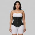 Woman wearing a black waist trainer over a white top and shorts on a gray background